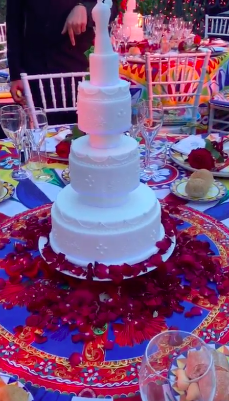 A giant three-tiered cake in the center of a table is surrounded by flower petals