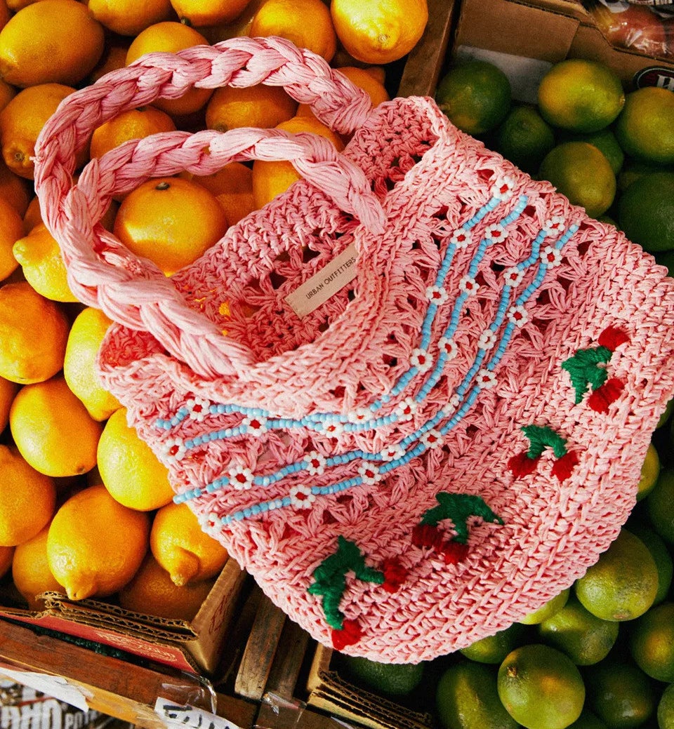 a pink straw woven bag with blue and white floral beading and embroidered cherries