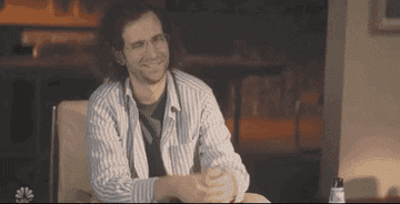 Kyle Mooney shrugging as he wears a button-down and glasses