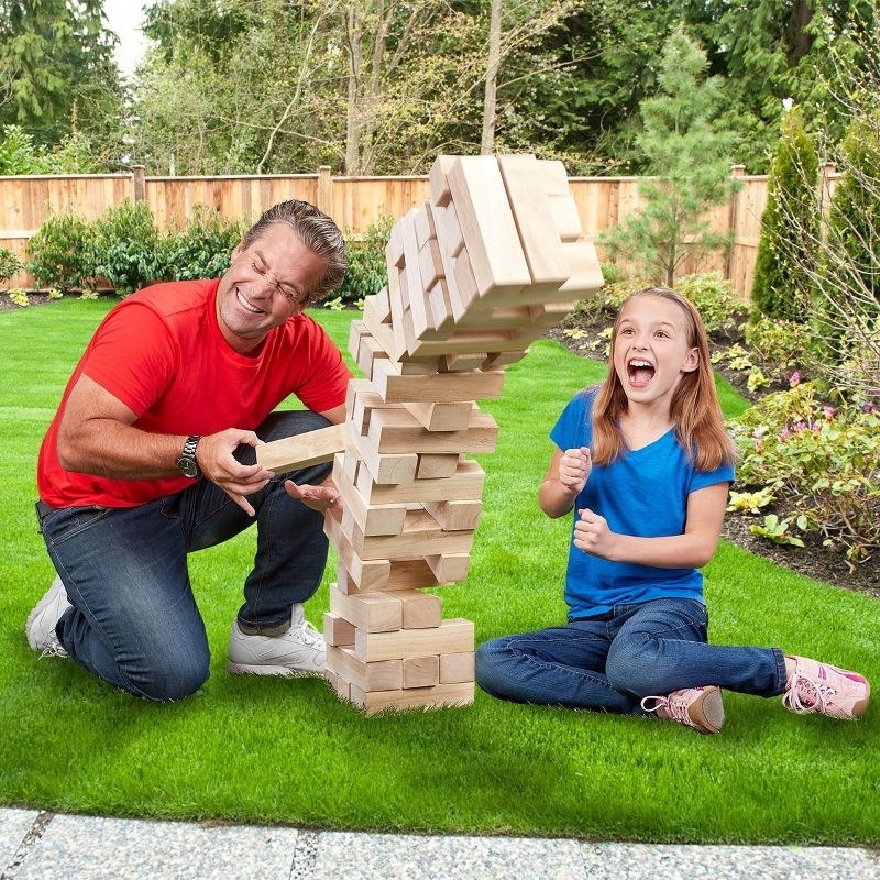 An adult and child model playing the game outside with adult pulling a wooden block out from the middle of the stack
