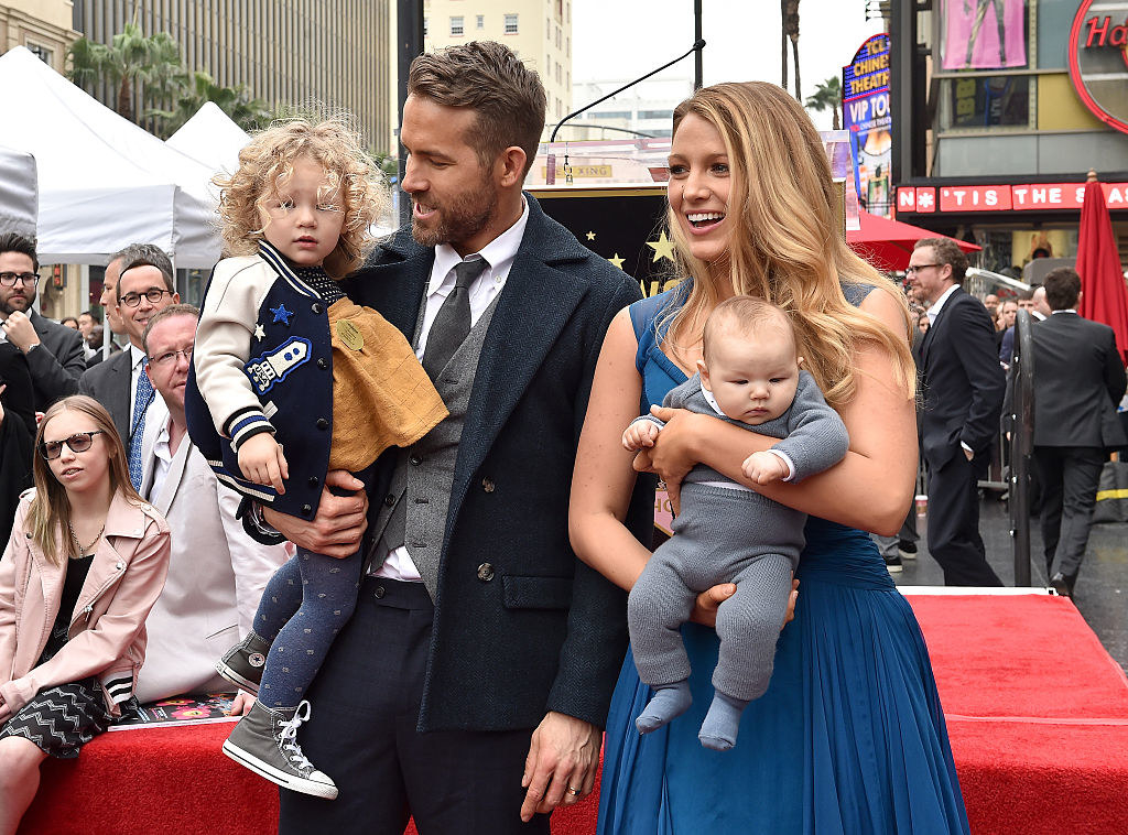 Ryan Reynolds wears a dark suit, James Reynolds wears leggings with a letterman jacket, Ines Reynolds wears a onesie, and Blake Lively wears a sleeveless gown