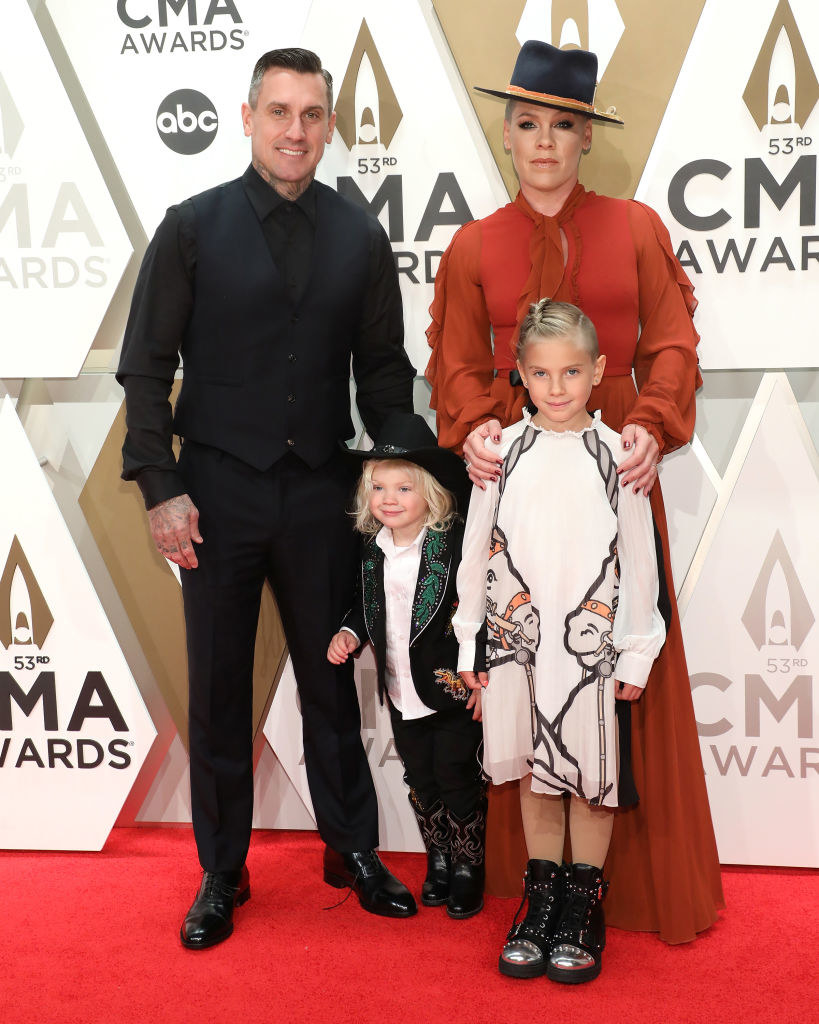 Carey Hart wears a dark suit, Jameson wears a dark suit with a light button up shirt, Willow wears a long sleeve dress with sheer sleeves and P!nk wears a light colored gown