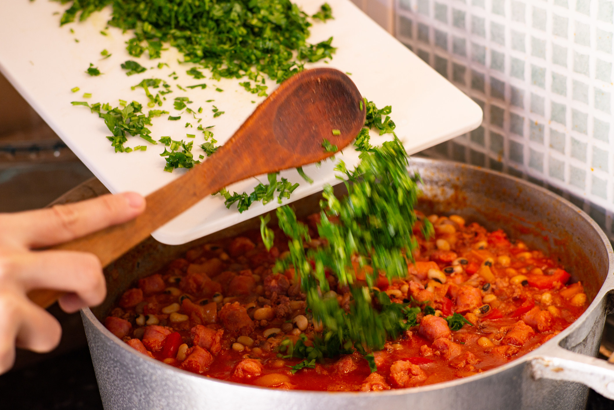 Putting fresh herbs into a pot of chili.