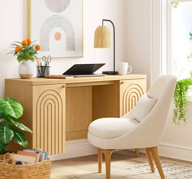 Desk styled with various office supplies next to a white upholstered chair