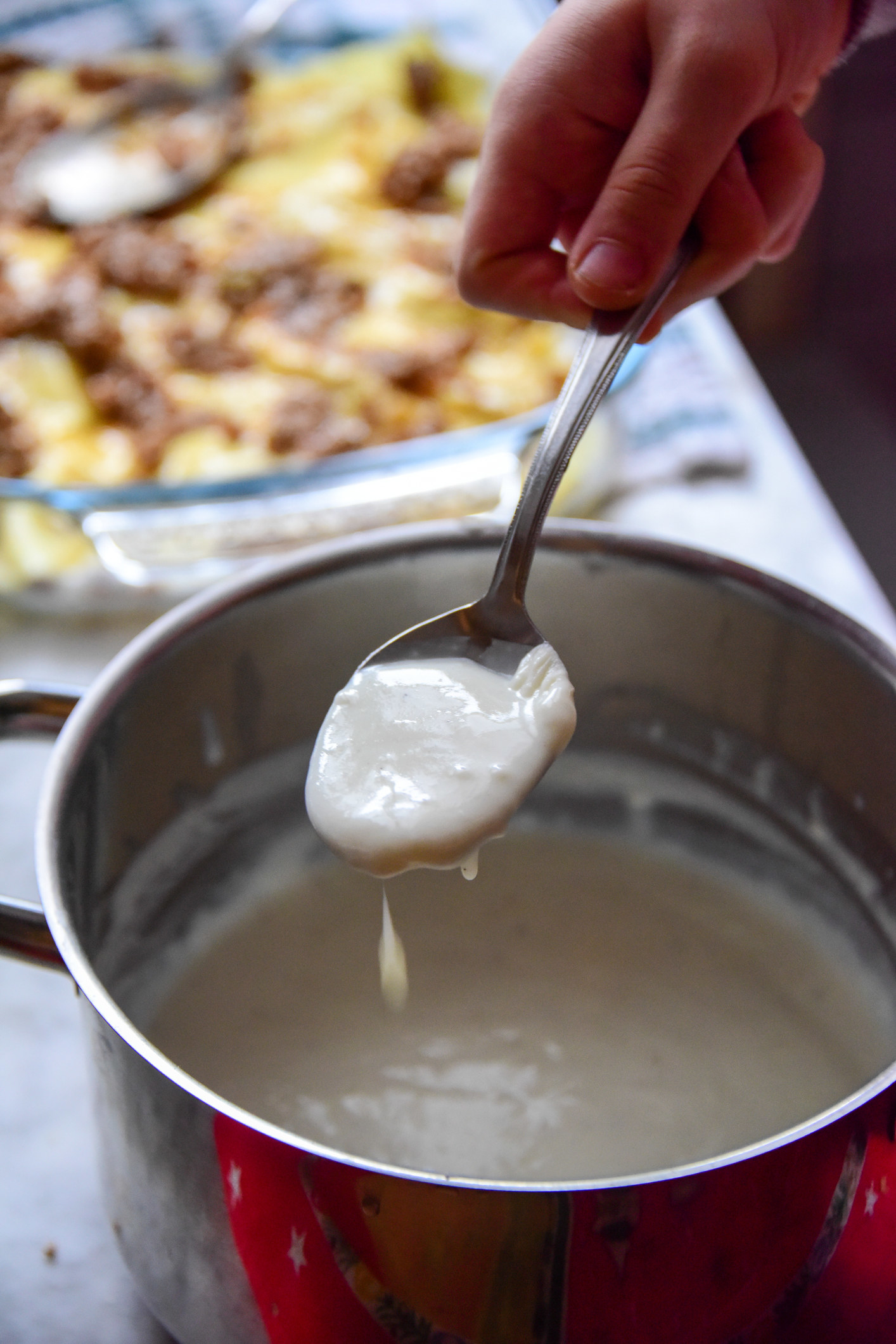 A person holding a spoonful of bechamel sauce.