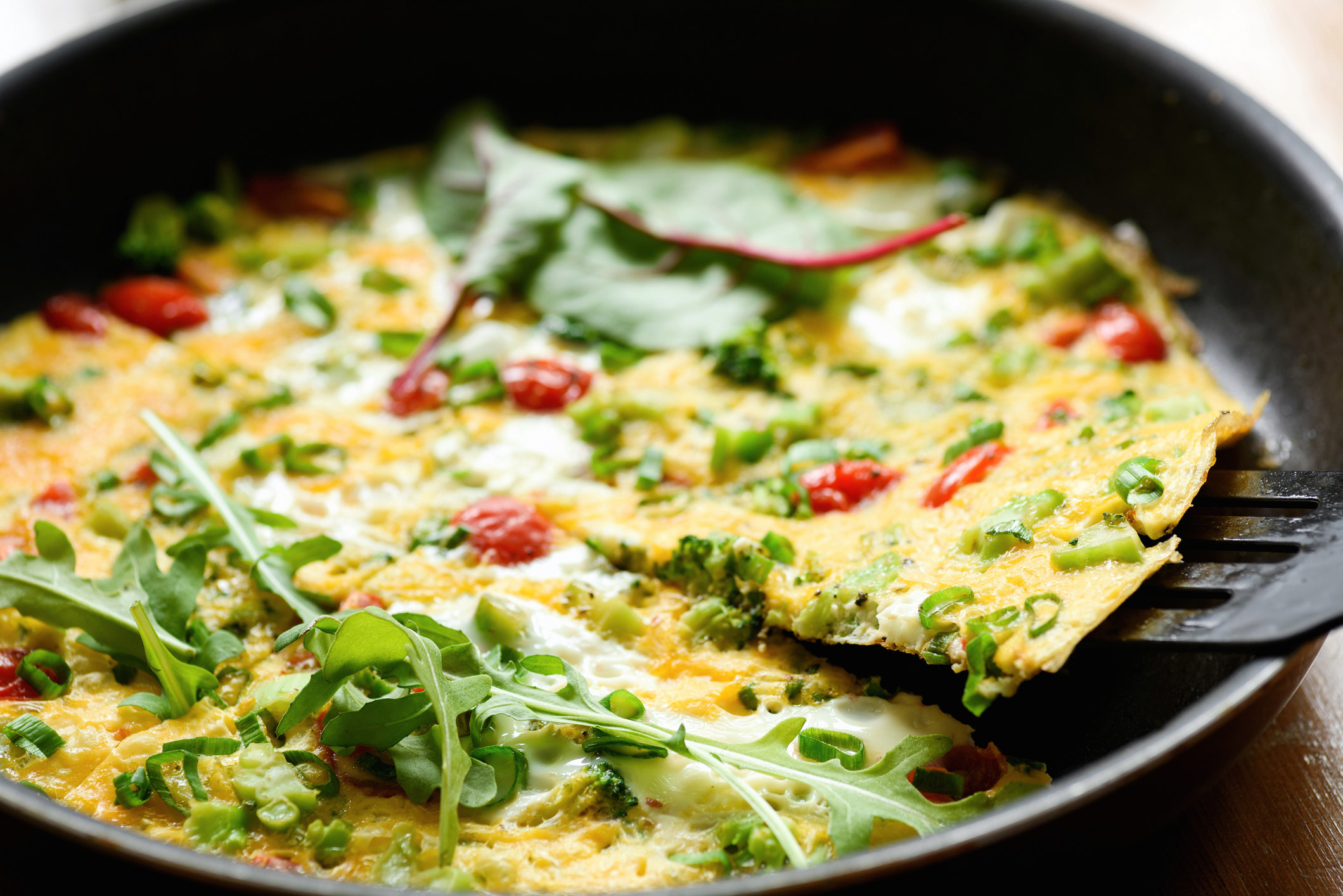 A frittata with cherry tomatoes, greens and cheese.
