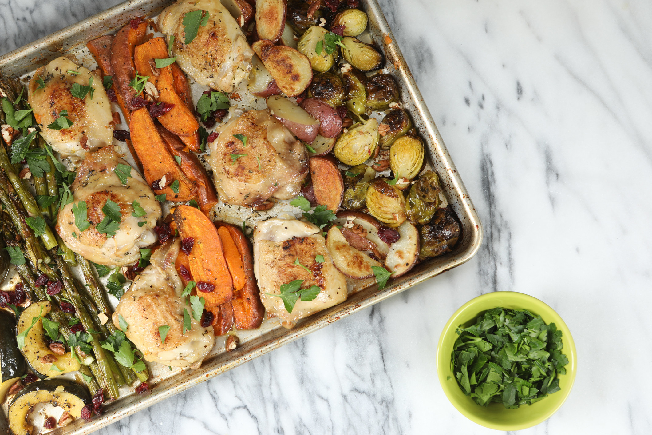 Sheet pan chicken with lots of vegetables and a side of fresh herbs.