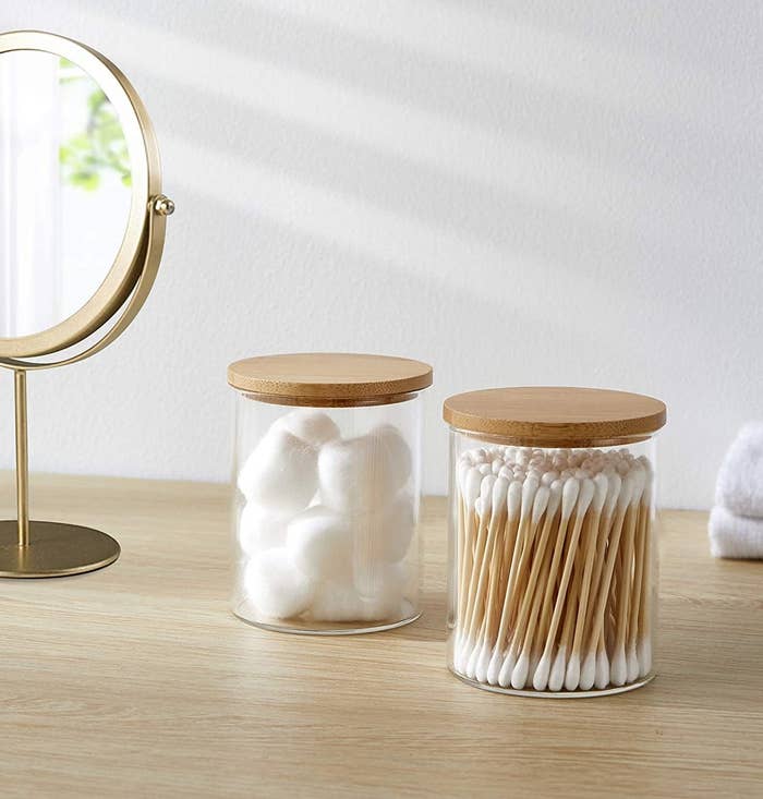 two glass jars with bamboo lids holding cotton balls and swabs
