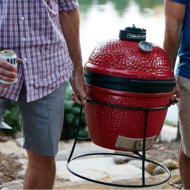 Two people carrying a red portable grill