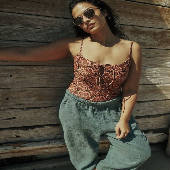 Different model wearing the suit with green balloon pants over them and lounging against wooden fence