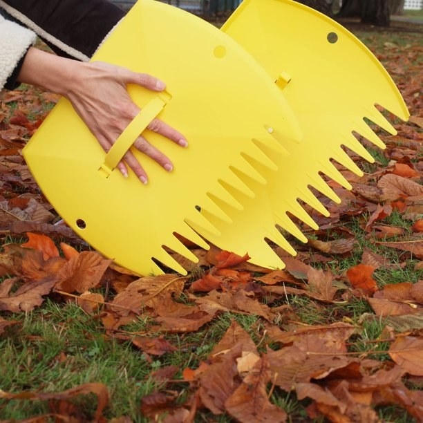 Person using yellow leaf scoops to pick up leaves
