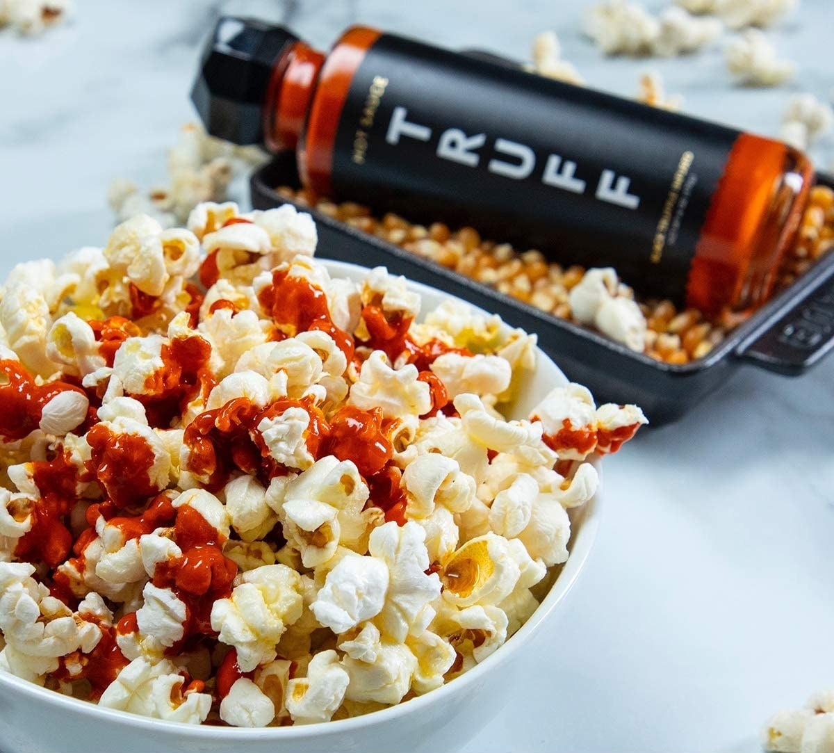 Some of the sauce drizzled over a bowl of popcorn with the bottle in the background