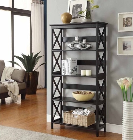 The black five-tier bookshelf holding books, candles and other decor