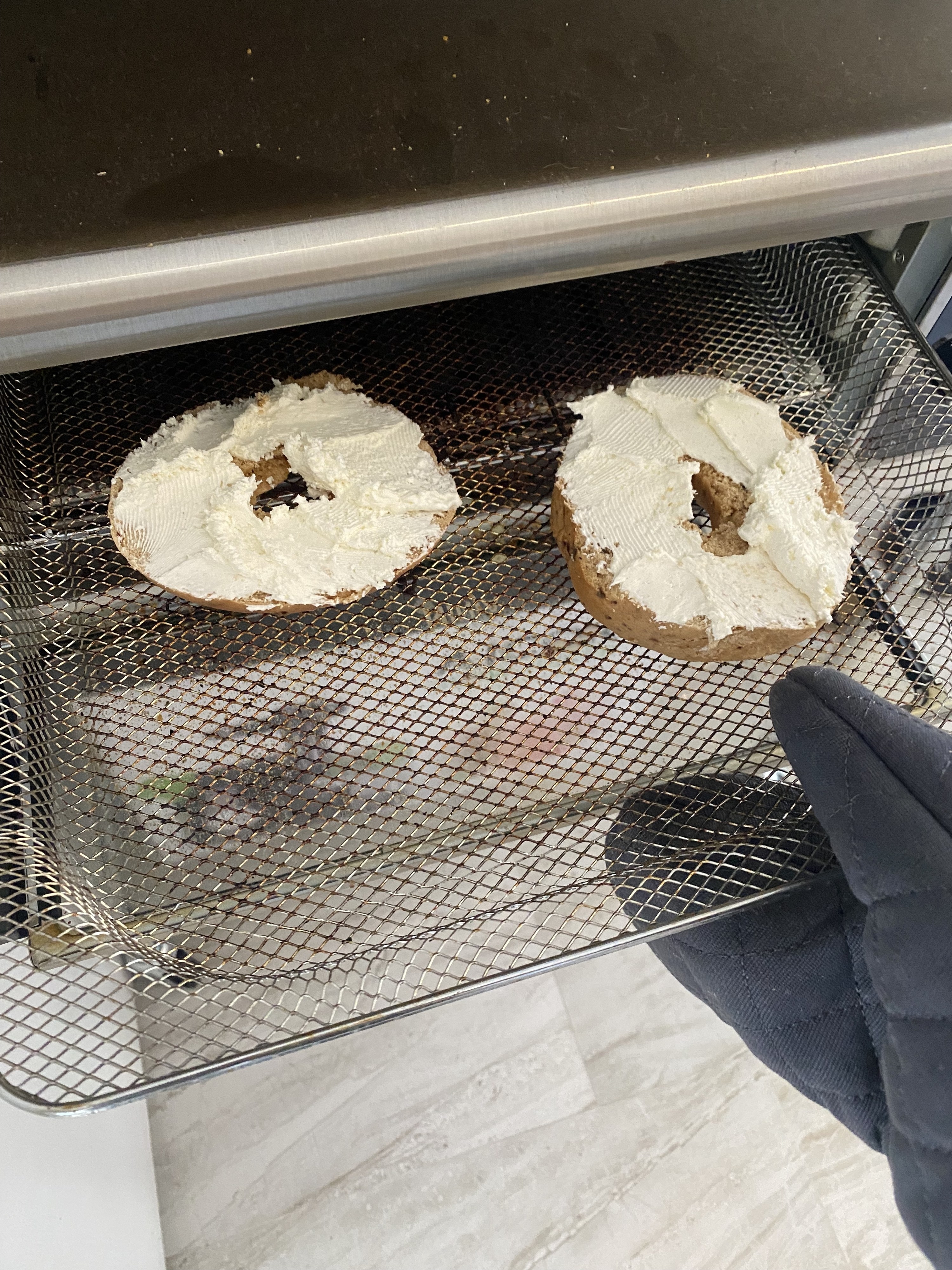 Two bagel halves covered with cream cheese on a rack