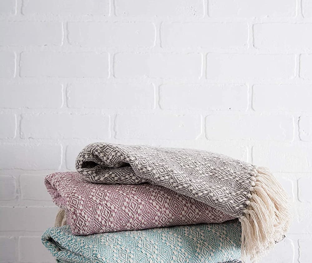 four throw blankets folded and stacked on a stool