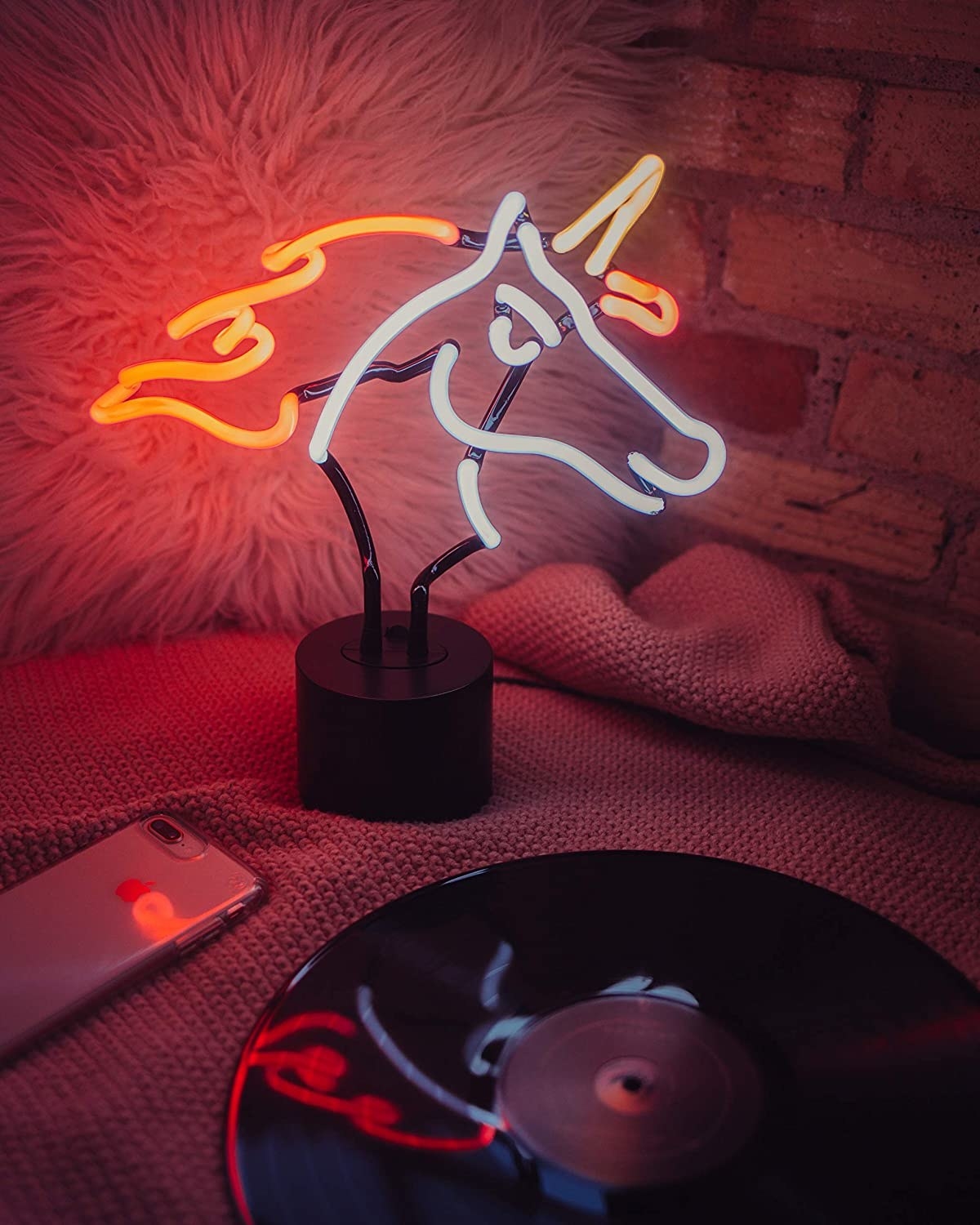 a unicorn-shaped neon light on a bed beside a phone and a vinyl record