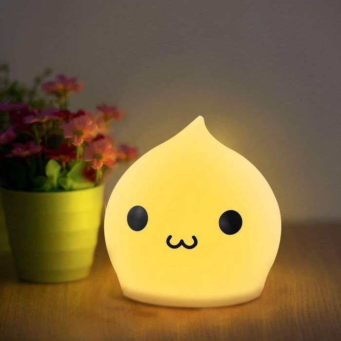 a cute night light with a little face on a table beside a plant