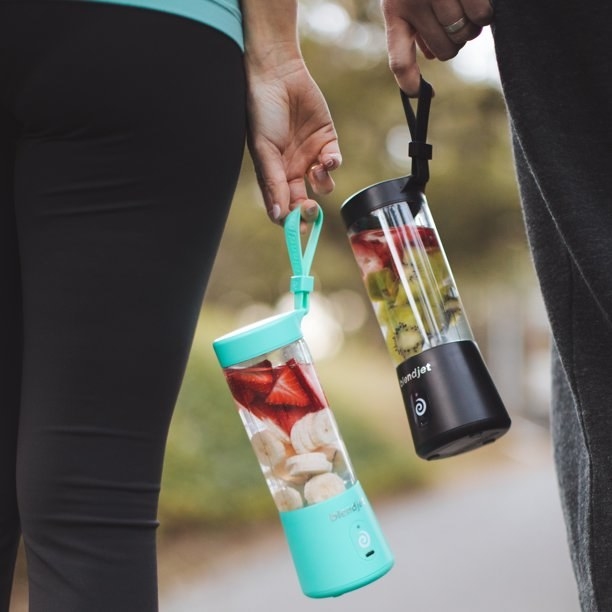 two models holding the mint and black portable blenders full of fruit