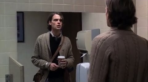 Reid staring at himself in the mirror while carrying a bag and coffee
