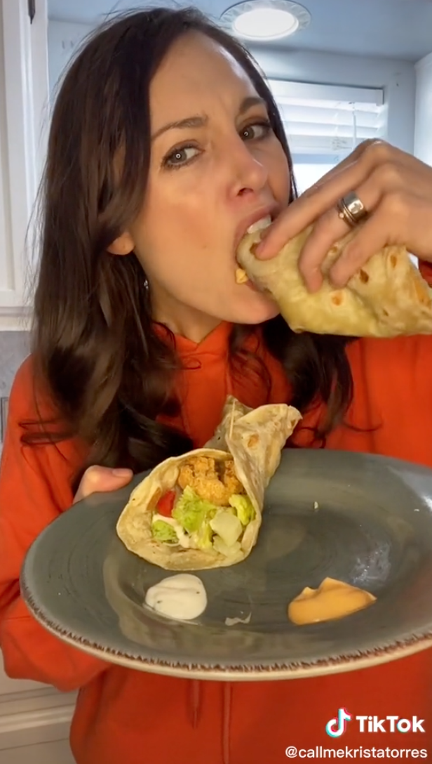 Woman eating a snack wrap with one hand while holding a plate containing another wrap with the other hand