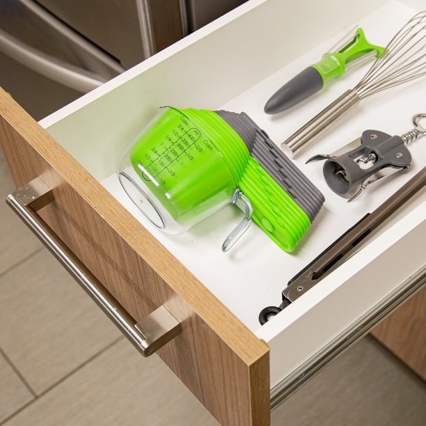 the grey and green cups in a drawer with other kitchen tools