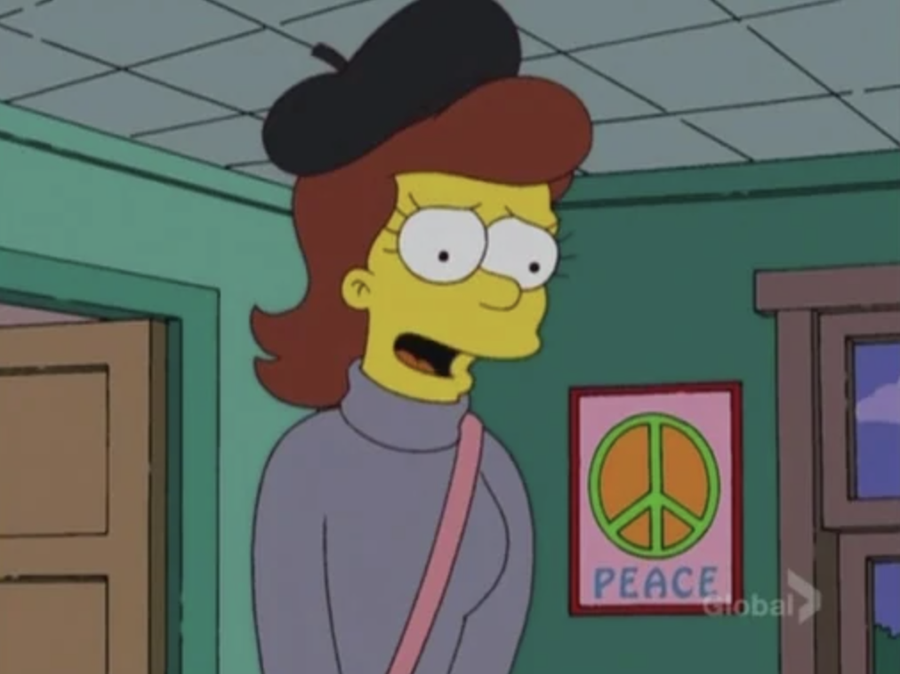 A young woman wearing a beret stands in a room, there&#x27;s a &#x27;peace&#x27; poster hanging on the wall behind her