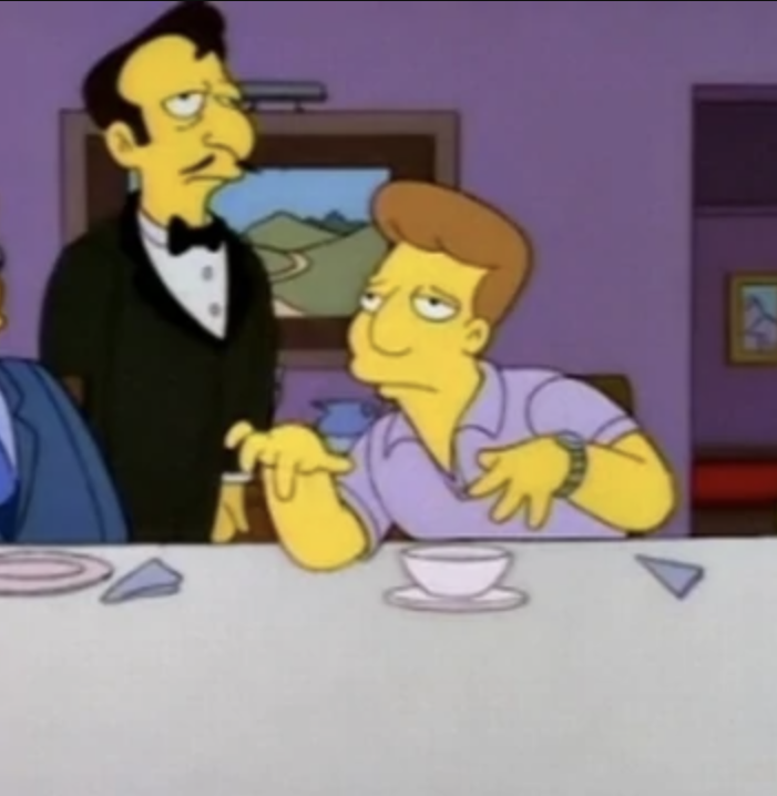 A waiter in a suit stands at attention, while Freddy sits at a table making a face and a funny hand gesture