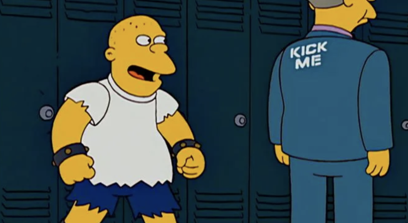 Kearney stands in a school hallway, laughing at Principal Skinner who has &#x27;kick me&#x27; written on his back