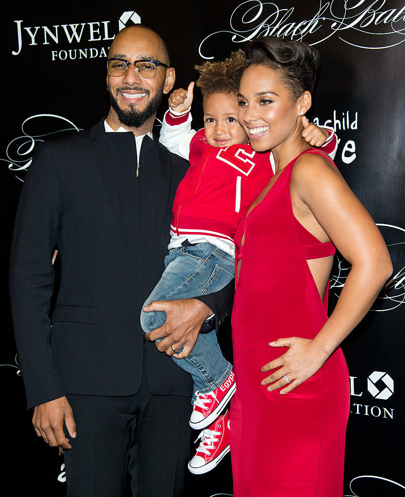 Swizz Beatz wears a dark suit, Egypt wears jeans with a brightly colored letterman jacket, and Alicia Keys wears a sleeveless brightly colored gown