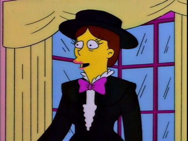 Shary Bobbins stands in the Simpsons&#x27; living room, she&#x27;s wearing a broad brimmed black hat, a suit and a purple bow tie