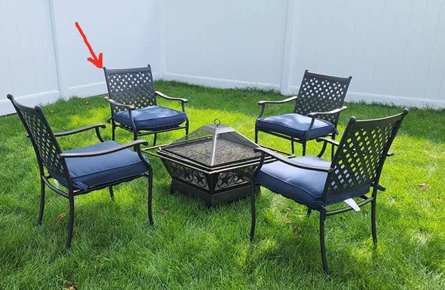 Reviewer image of four black wrought iron metal chairs with blue cushions on grass around a fire pit