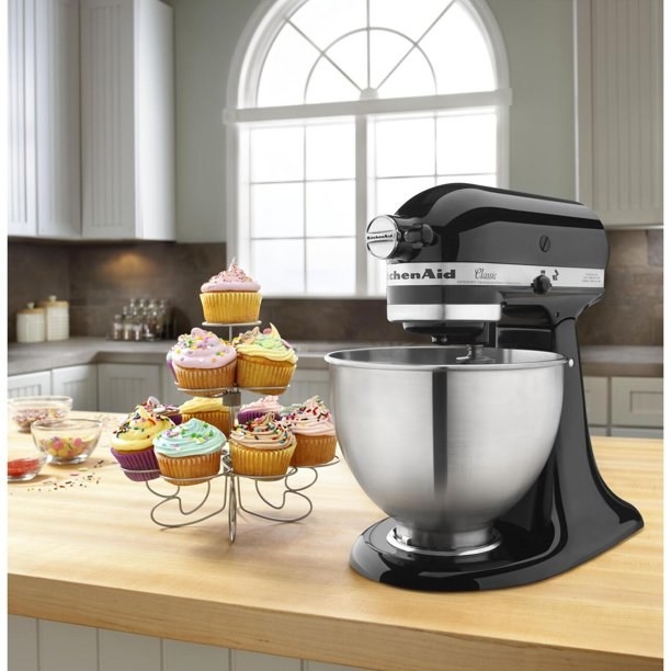 the black mixer on a counter with a stand of cupcakes