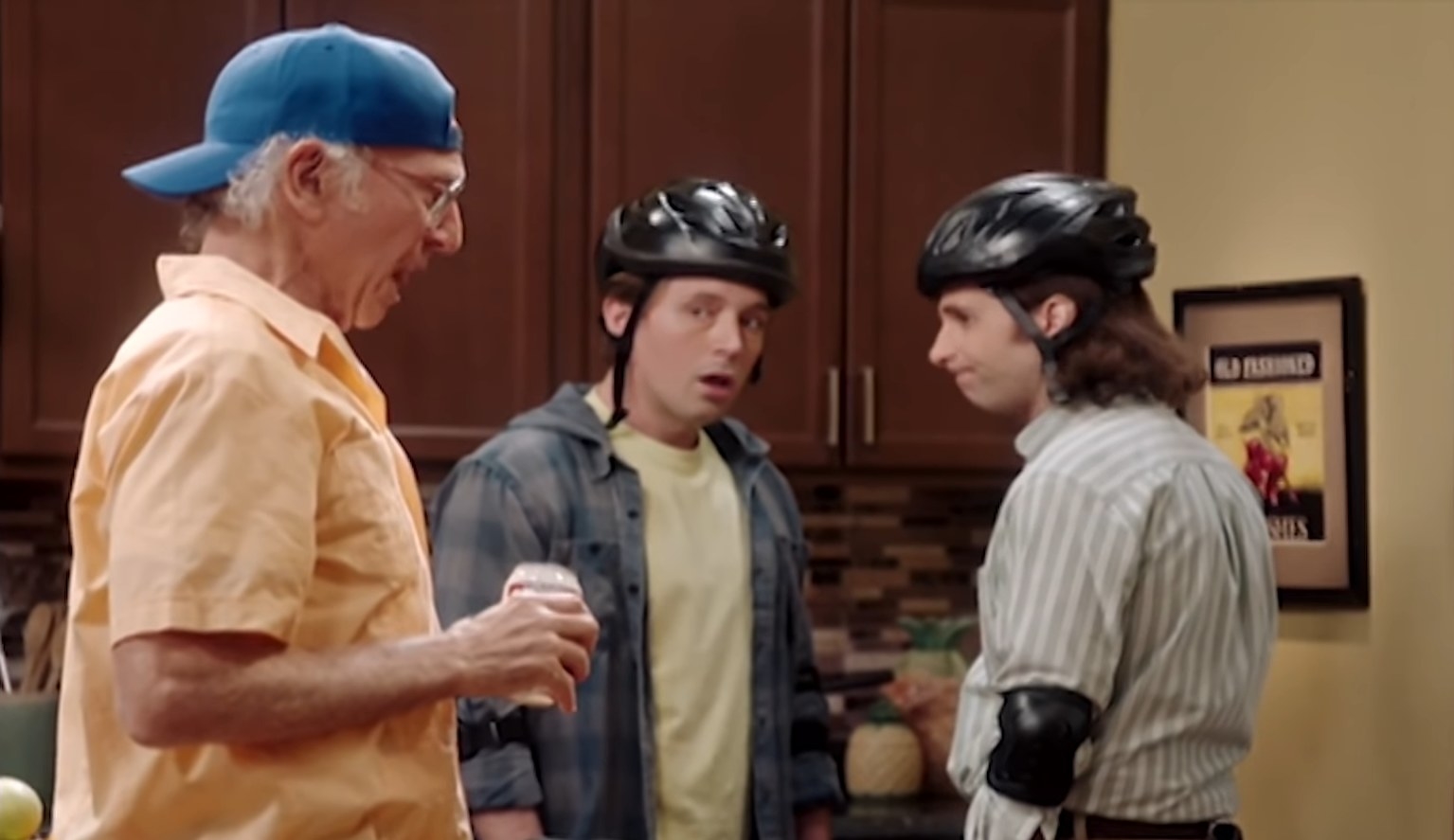 Kyle Mooney and Beck Bennett wearing helmets and elbow pads while Larry David burps loudly