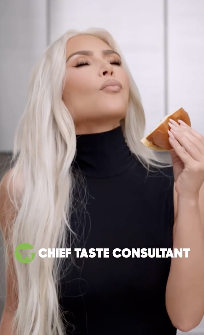 Kim holds up a half of a burger, pretending to eat, with the text from the promotional video reading &quot;chief taste consultant&quot;