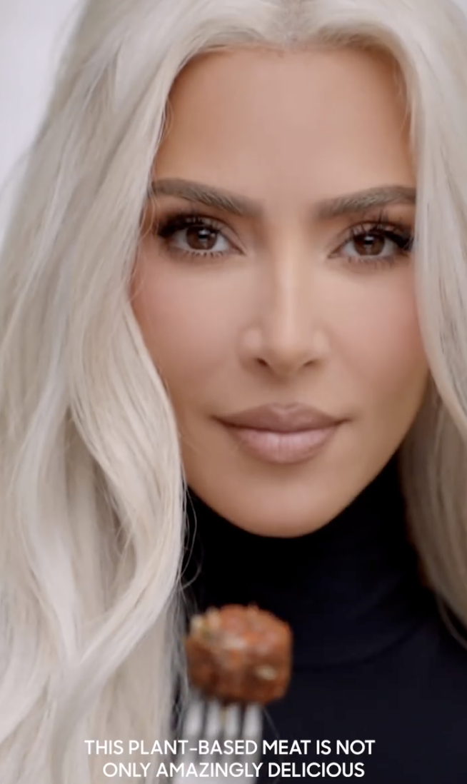 A close-up of Kim&#x27;s face as she holds up a Beyond meatball on a fork in a promotional video, with the caption reading, &quot;this plant-based meat is not only amazingly delicious&quot;