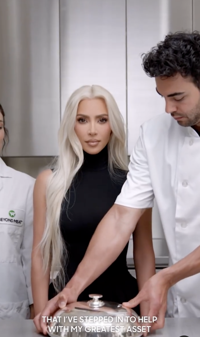 Kim Kardashian faces the camera between two people dressed as chefs in a Beyond Meat ad, with the subtitle reading &quot;i&#x27;ve stepped in to help with my greatest asset&quot;