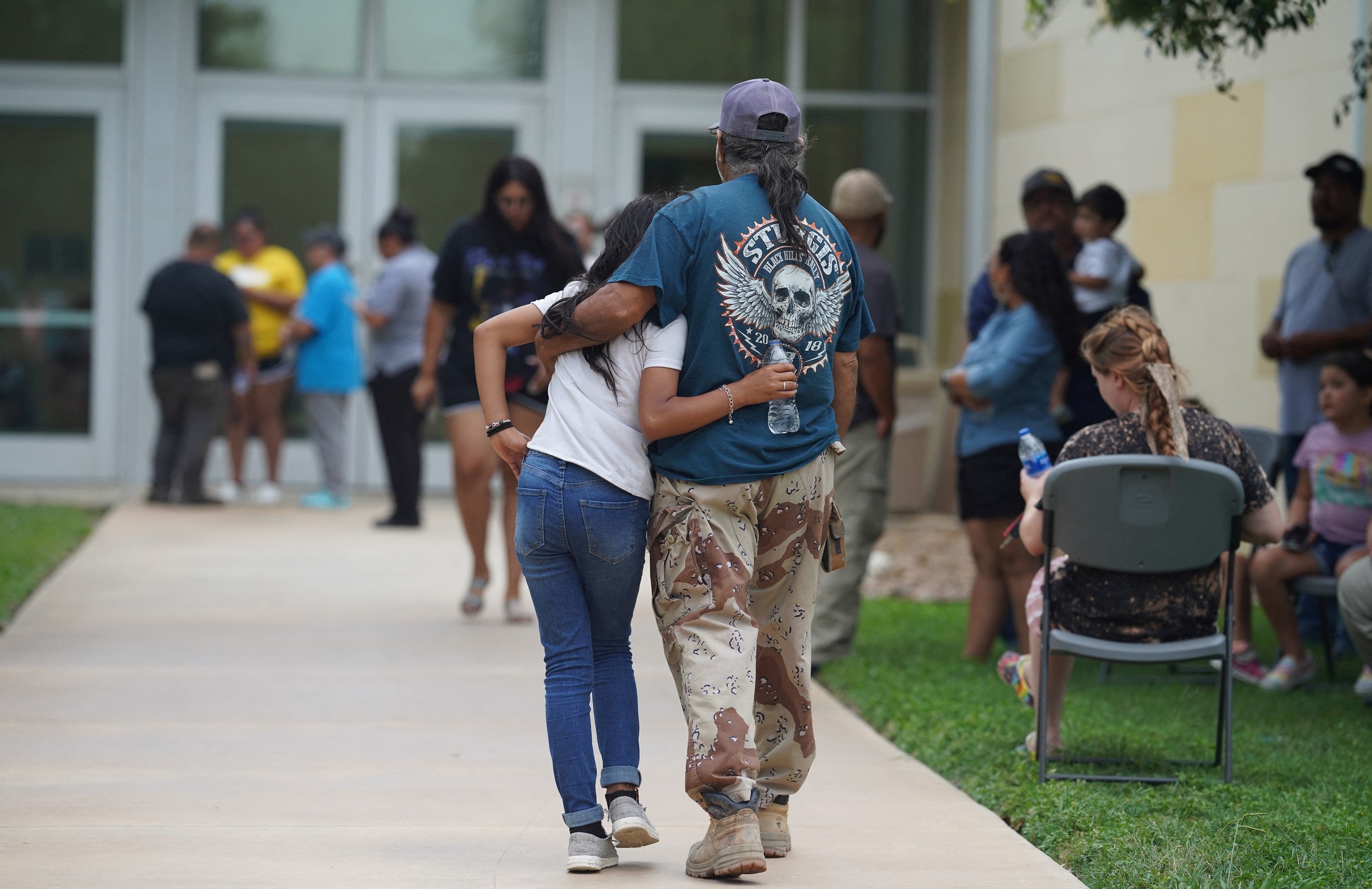 A young girl and man hold each other as they walk toward the double doors of a civic center, around which other people are gathered