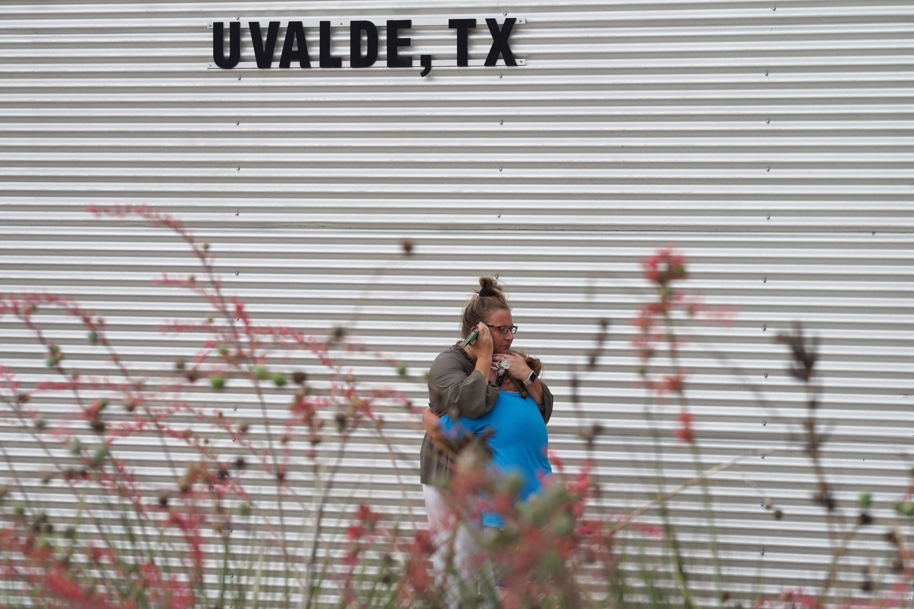 A mother hugs a child under a sign reading &quot;Uvalde, Texas&quot;