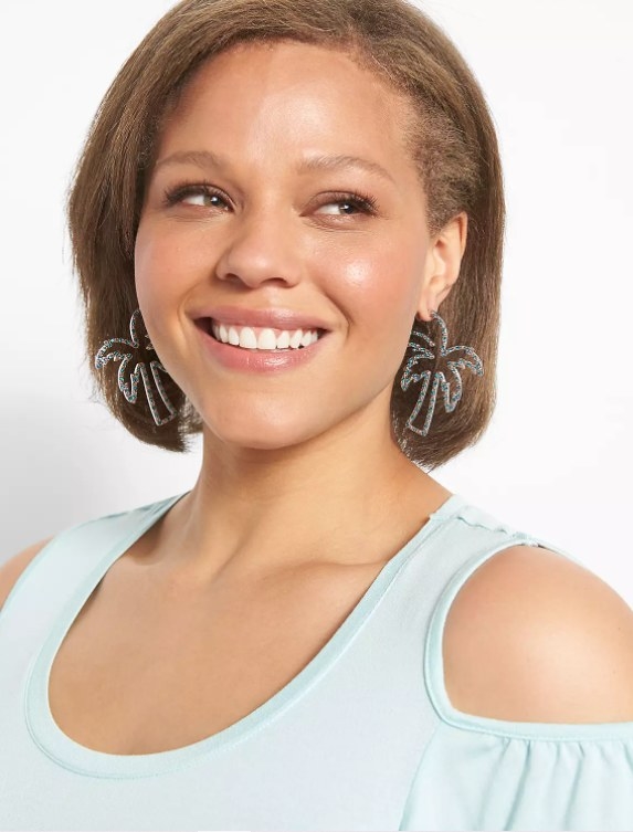 An image of a model wearing a pair of palm tree statement hoop earrings