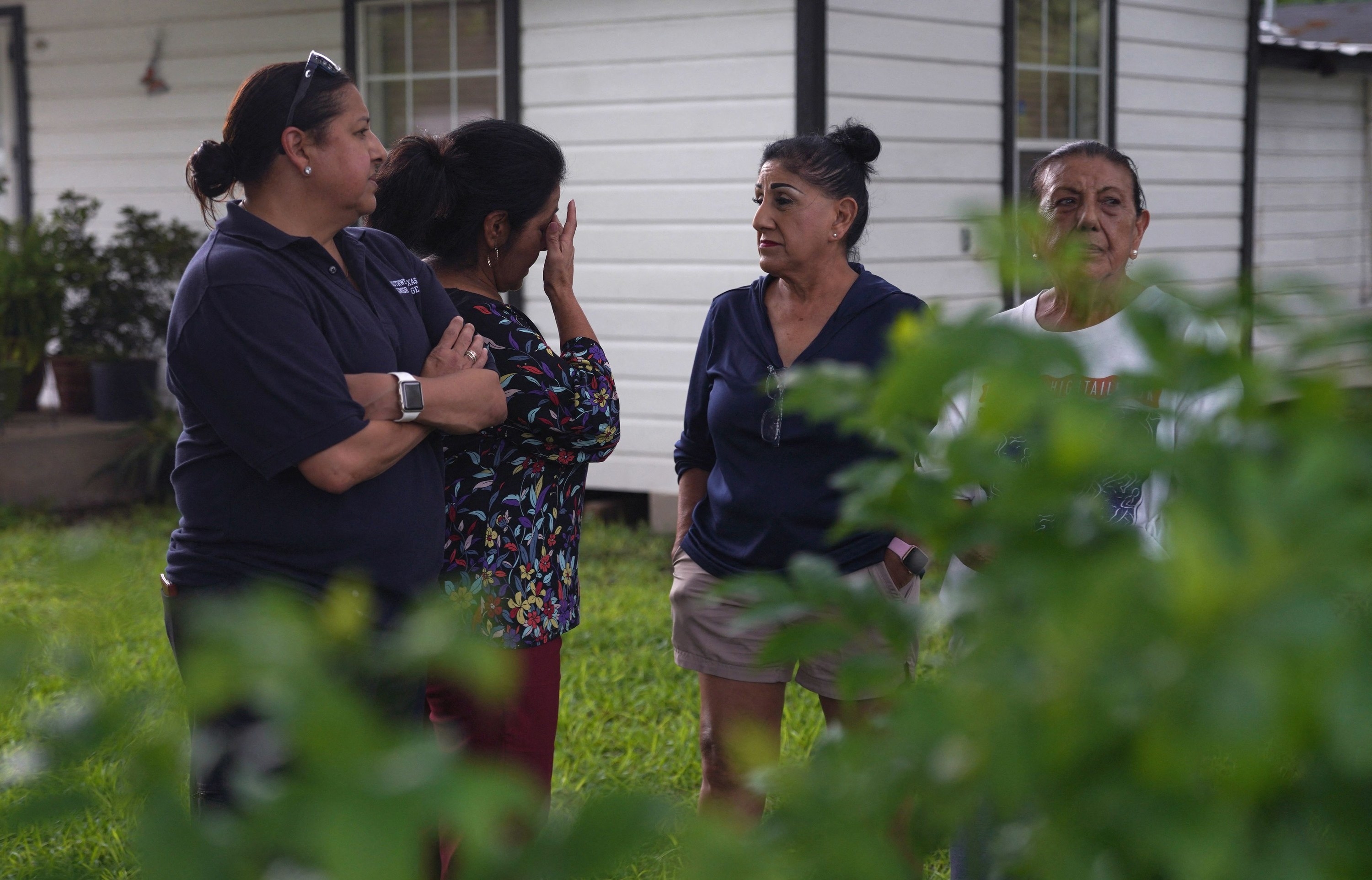 Four adults stand outside in a front yard as one wipes away tears