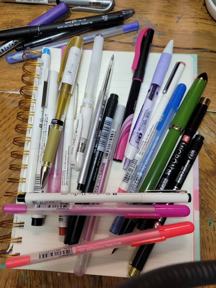 A bunch of pens piled upon a notebook