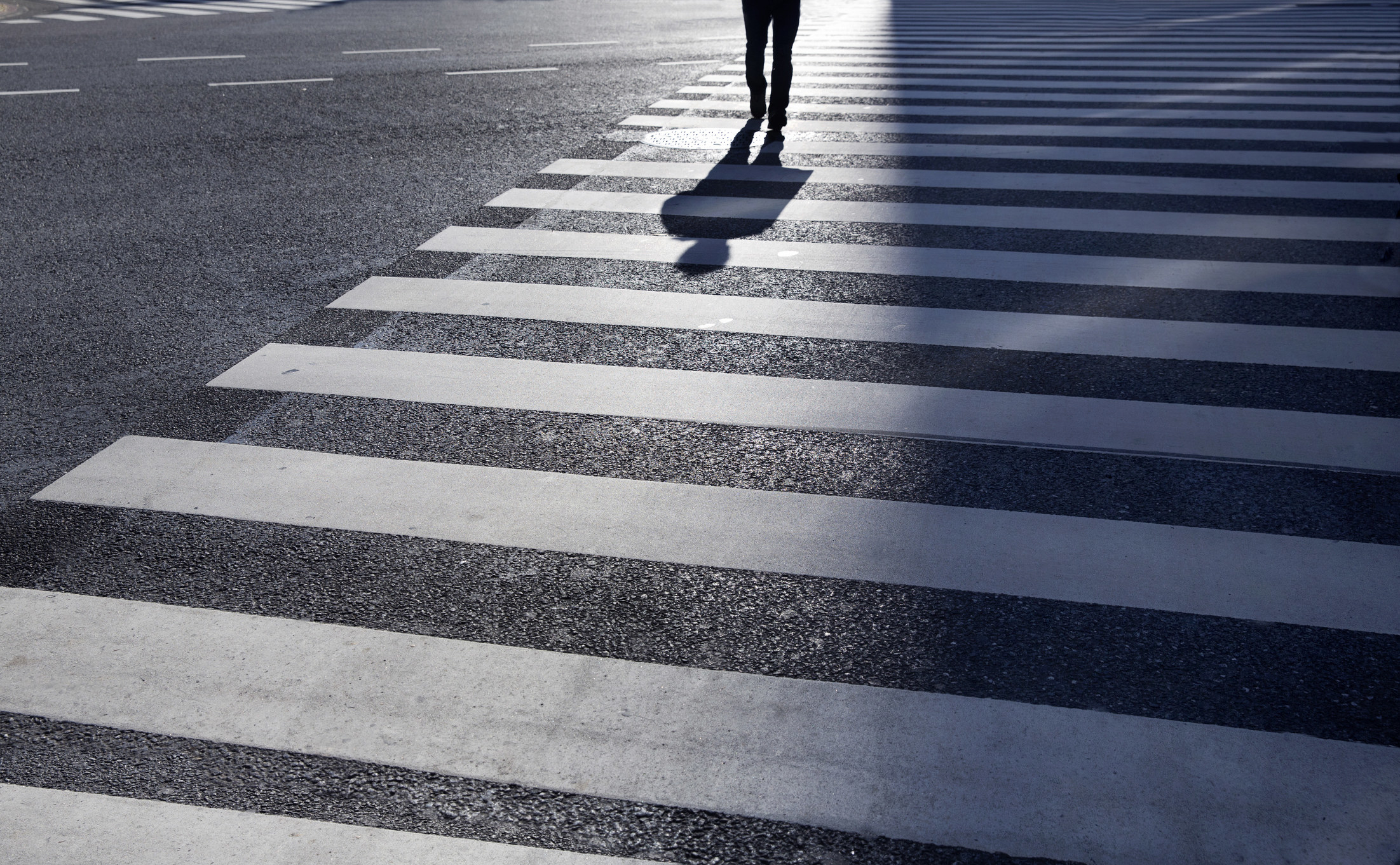 a crosswalk with a person&#x27;s shadow