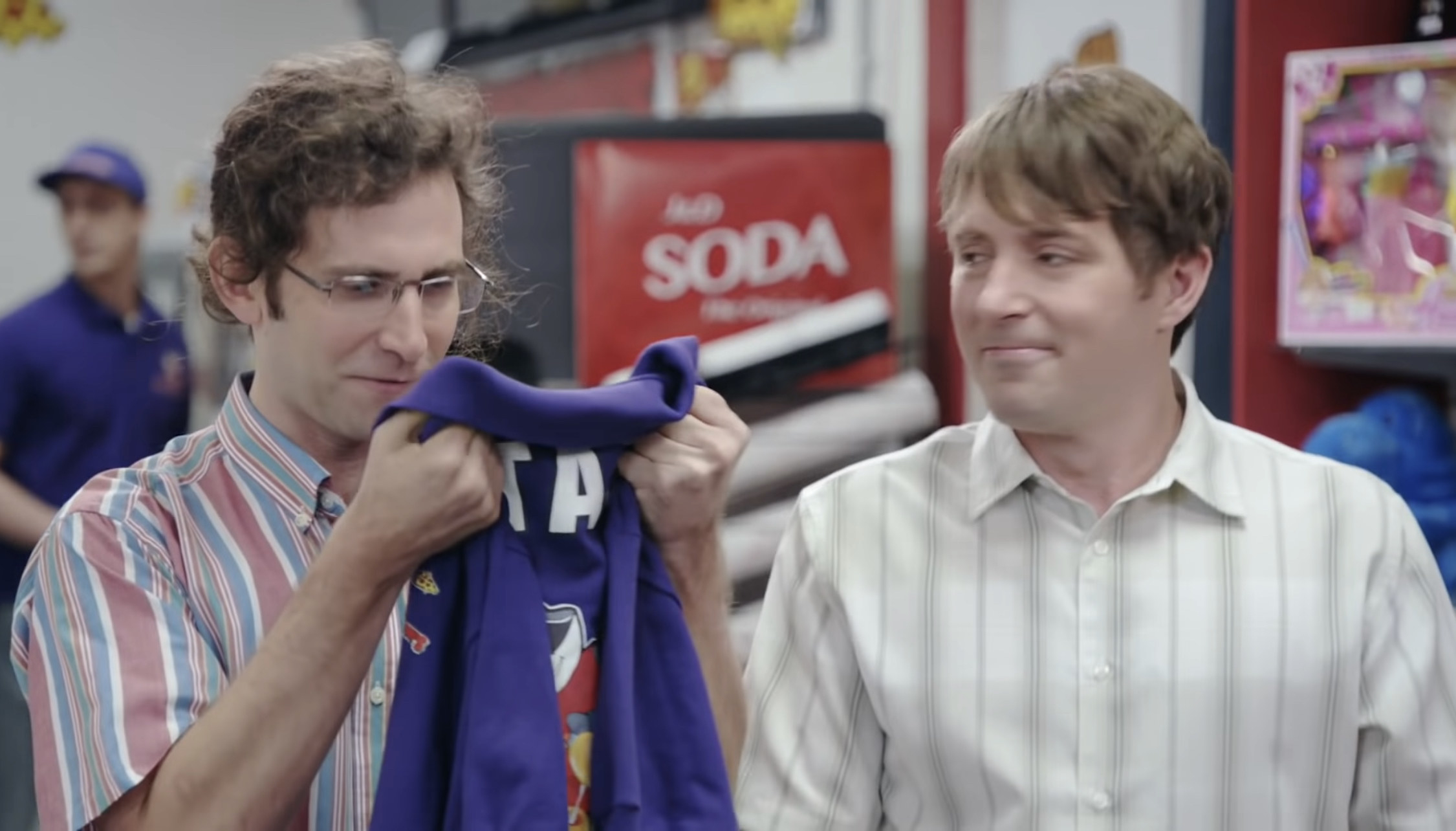 Kyle Mooney holds a Pogie Pepperoni&#x27;s shirt, staring at it awe