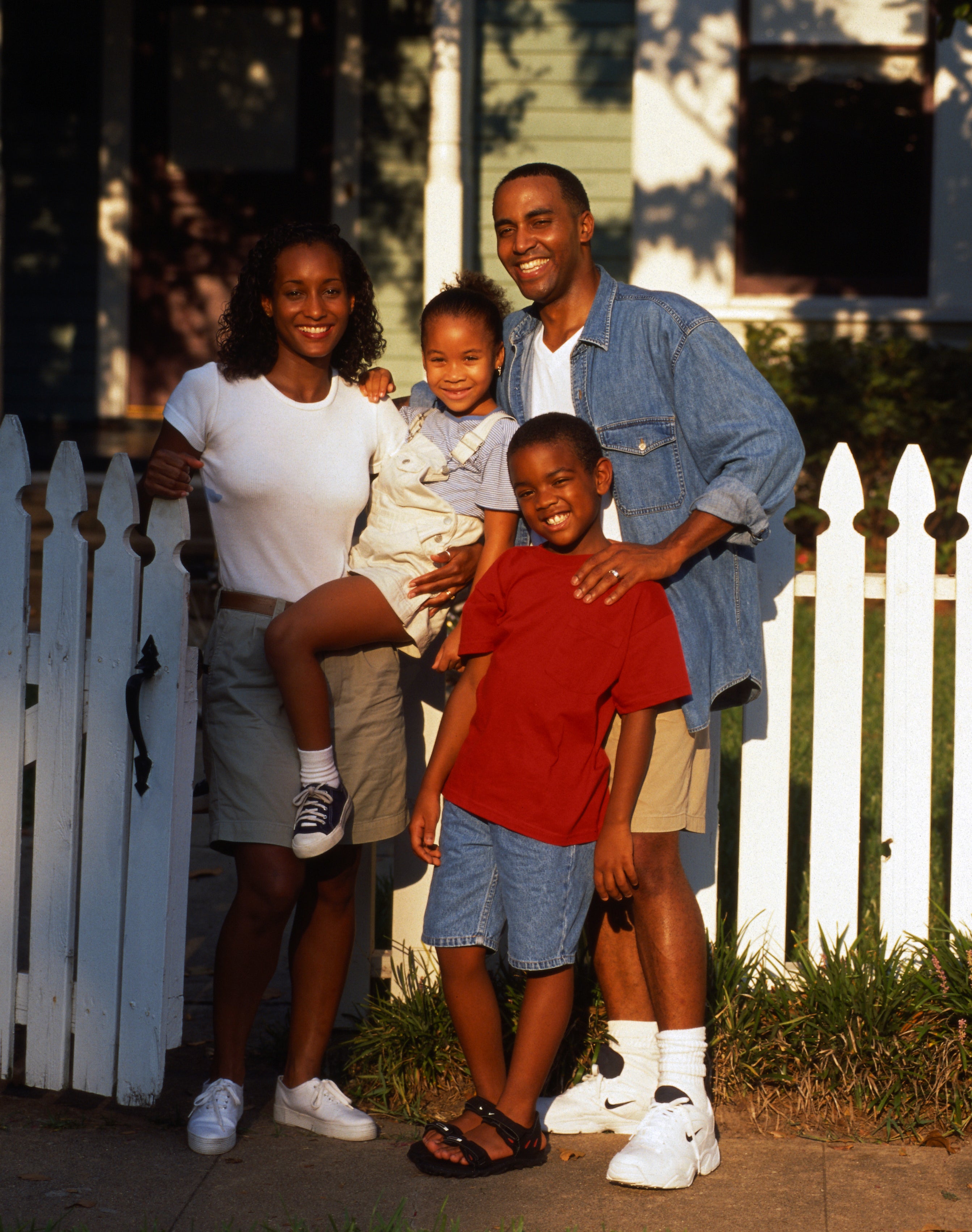 a family of four posing outside of their fenced house