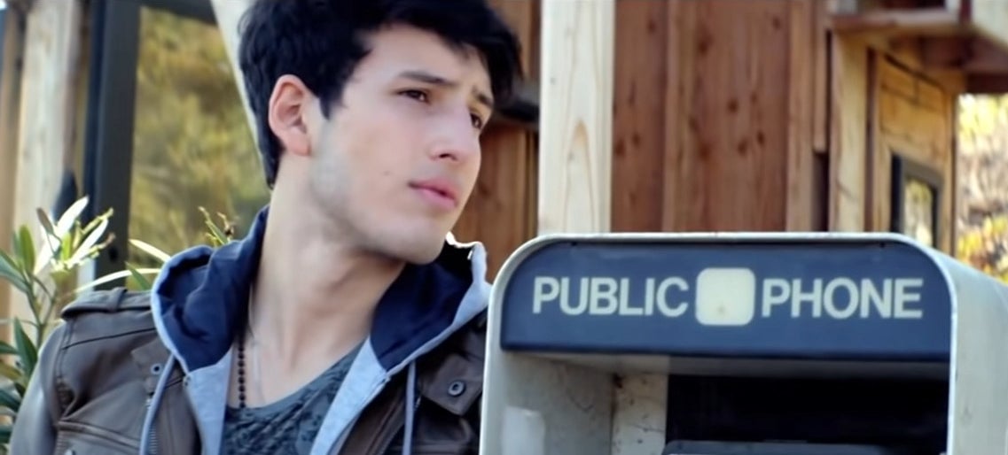 Sebastián in a leather jacket leaning on a public pay phone