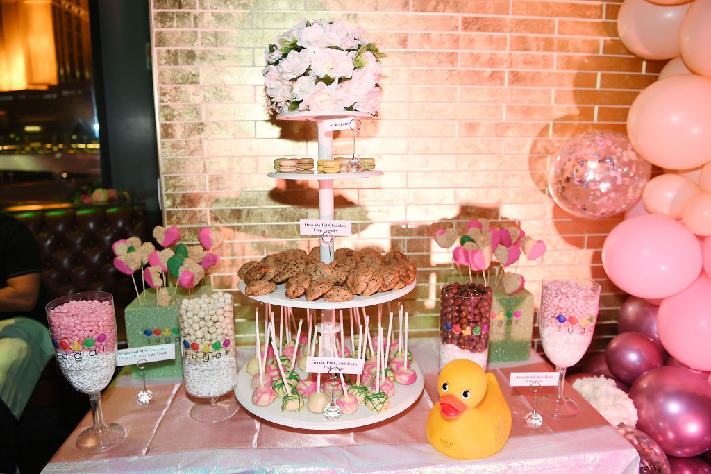 A table with various treats, including lollipops, cookies, and petit fours, along with flowers and balloons