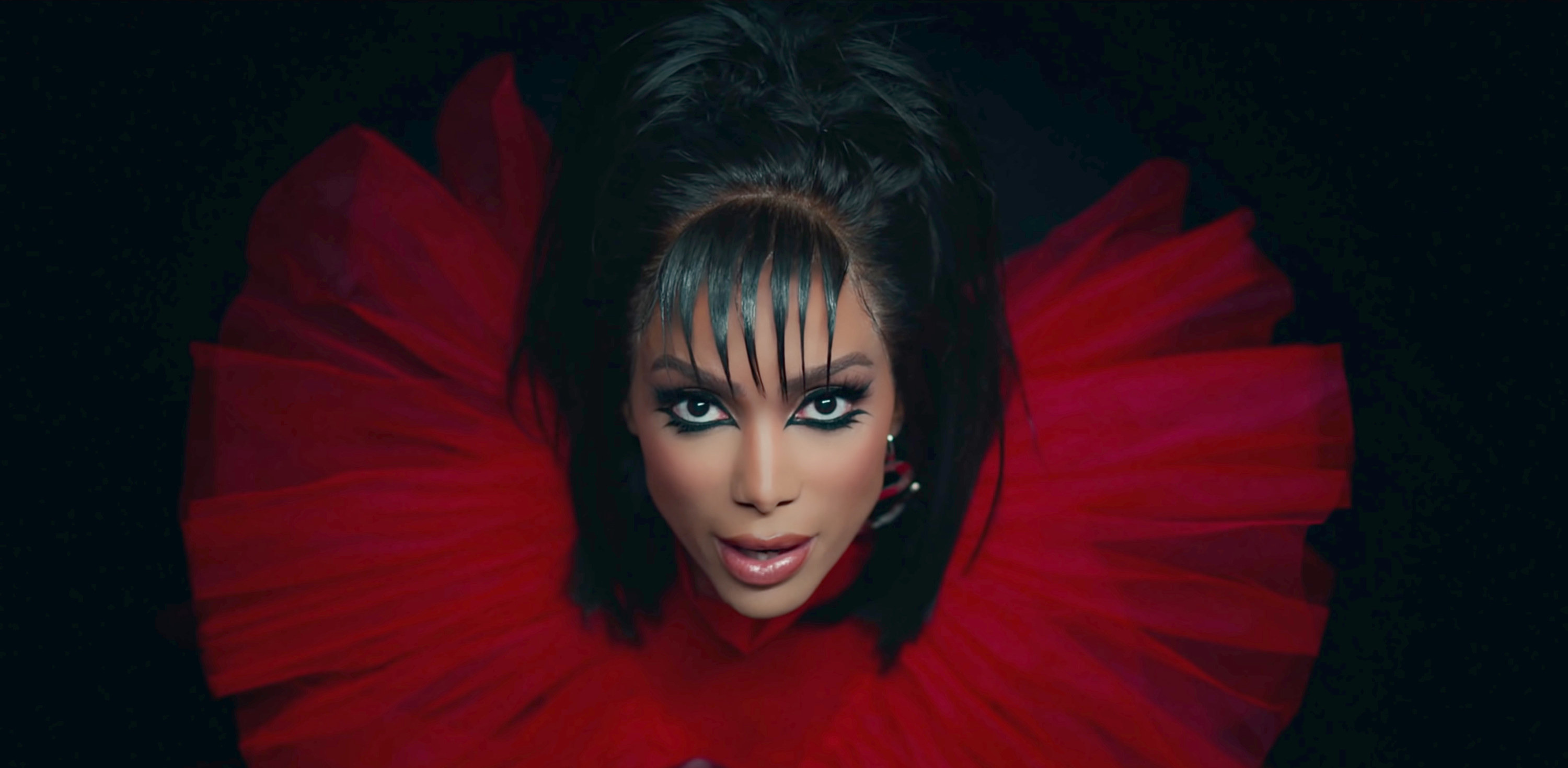 Headshot of Anitta with dramatic eye makeup and a wide, tulle neckpiece
