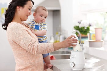 A parent holding a baby and using the bottle warmer