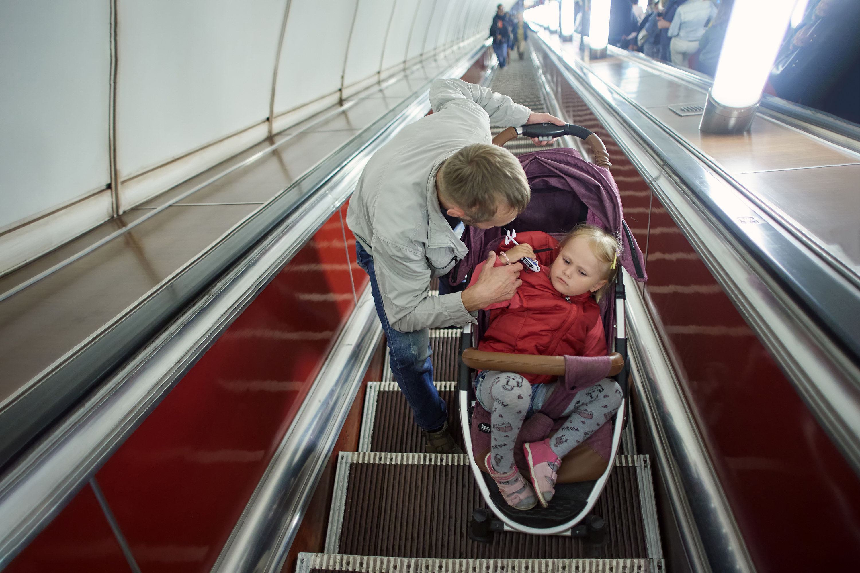 Little girl in baby carriage with father on escalator in subway