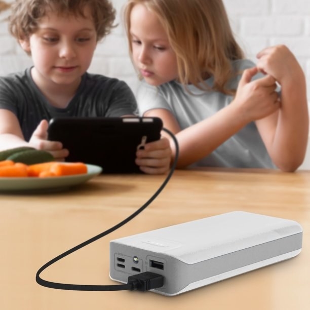 White portable charger plugged into tablet with kids playing on it